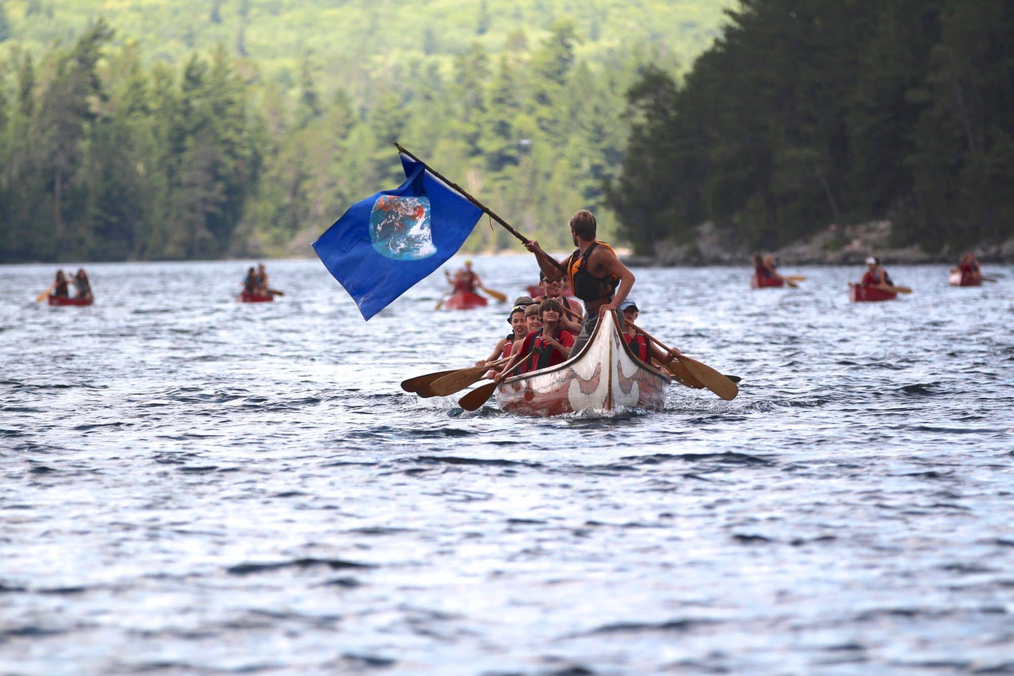Trip leader at front of canoe waving earth flag